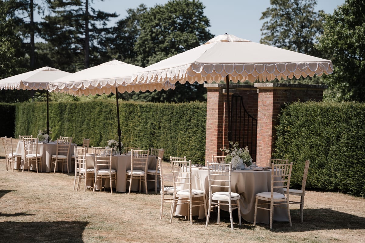 Round tables and chiavari chairs laid beneath scalloped parasols by the brick loggia