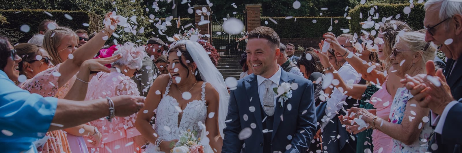 A bride and groom laughing as guests shower them with white confetti petals