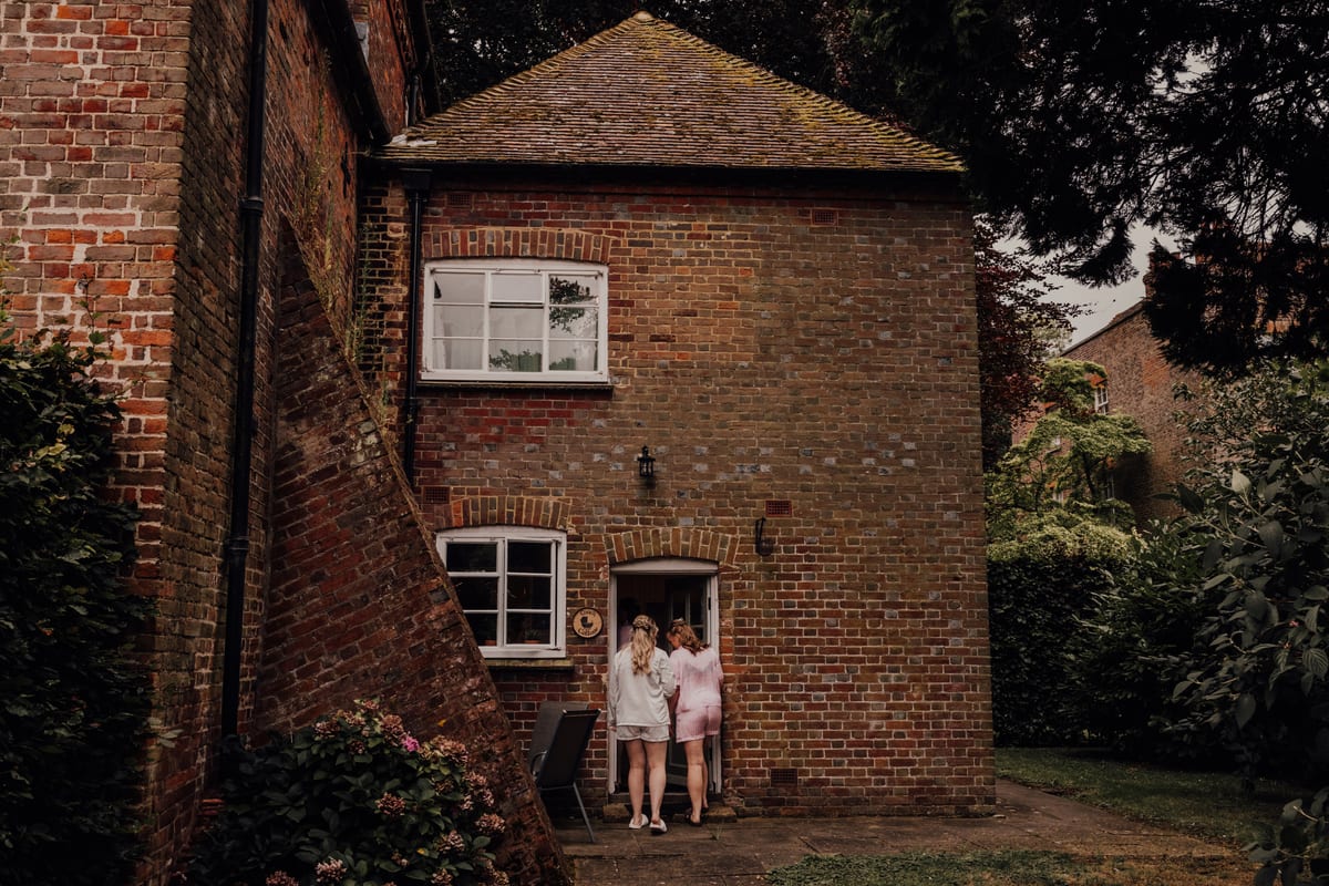 Bridesmaids in matching robes at the door of the brick Coach Cottage