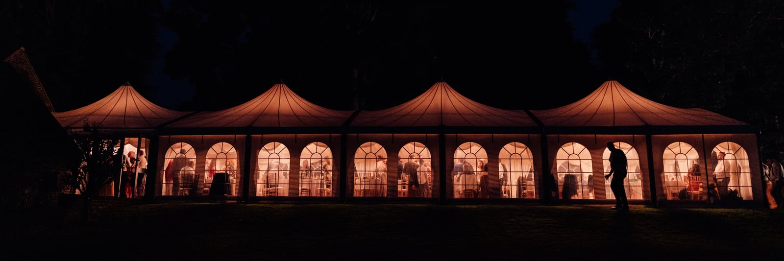The marquee glowing from within at night, guests silhouetted in its arched windows