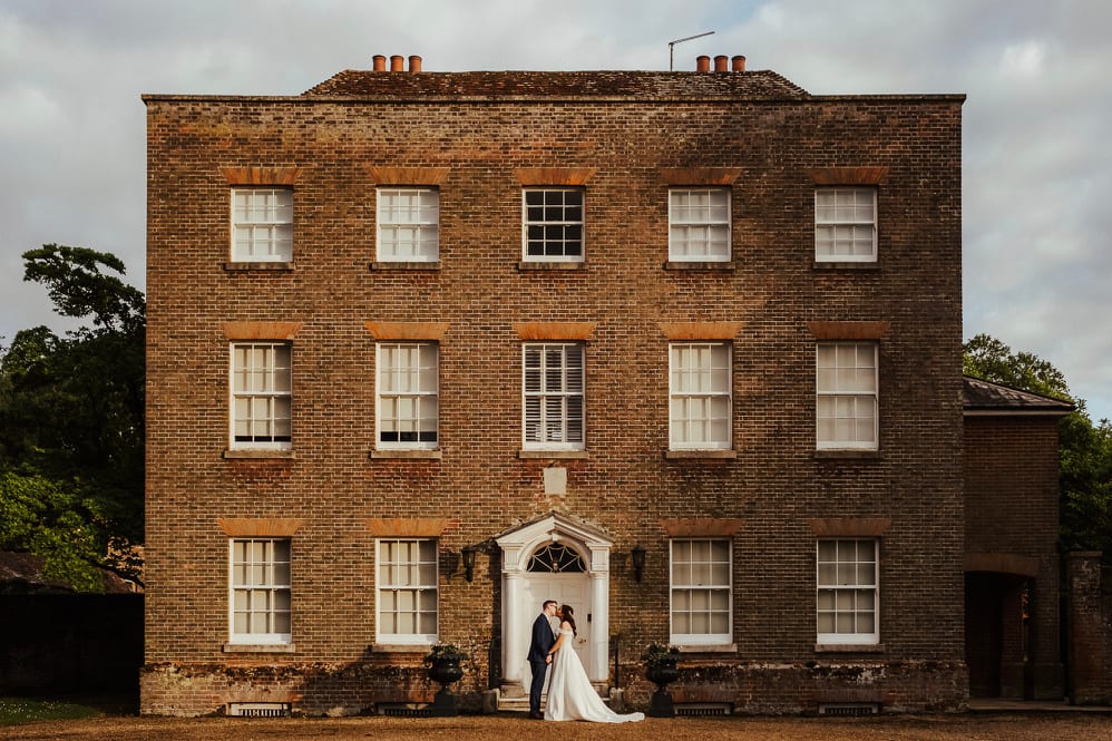 A couple embracing at the manor's pillared front door, beneath the Georgian brick façade