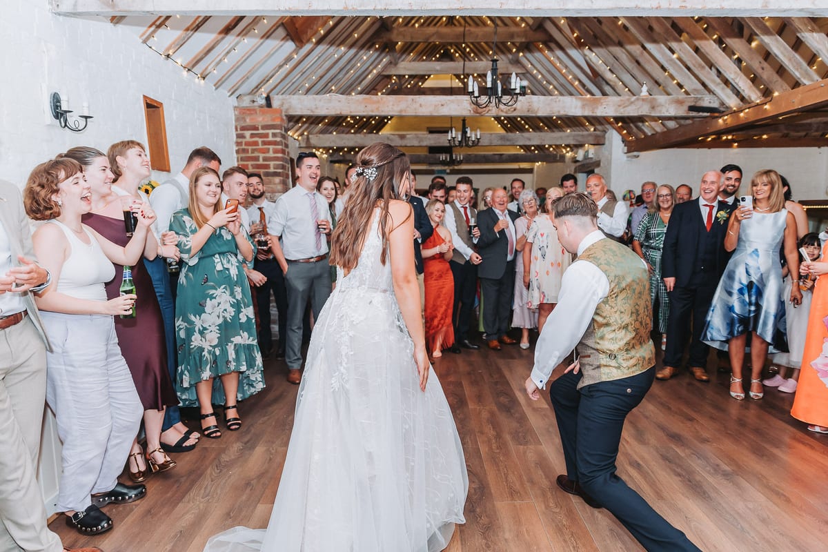 A bride and groom dancing in the barn, ringed by cheering guests